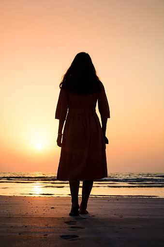 Girl walking on the beach at sunset back view