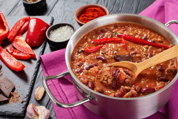 close-up of hot chili con carne hot delicious chili con carne with whole red hot chilis, kidney beans, tomatoes and piece of chocolate in a pot with ingredients at background, authentic recipe, view from above, close-up chili con carne photos stock pictures, royalty-free photos & images