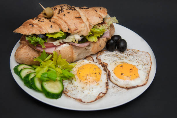 istock Breakfast on White Plate with Fried Eggs and Croissant with Fresh Vegetables over Black Background. 935941744
