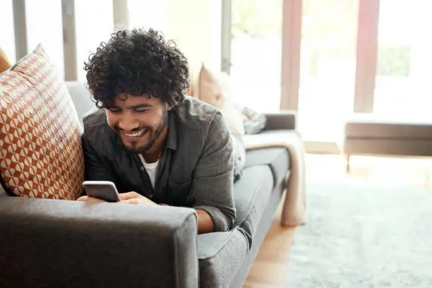 Shot of a handsome young man using his cellphone while relaxing on the couch at home