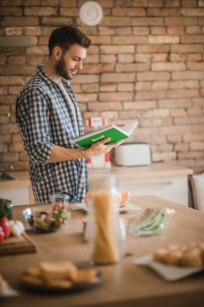 istock Young bachelor reading recipes from a cookbook in the kitchen. 935951844