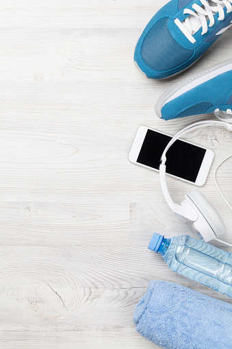 Fitness concept background with sneakers, headphones, water bottle and towel. Top view with space for your text