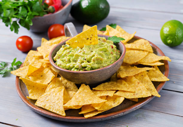 guacamole avocado, limetten, tomaten, zwiebeln und koriander, serviert mit nachos - traditionelle mexikanische snack - tortilla chip stock-fotos und bilder