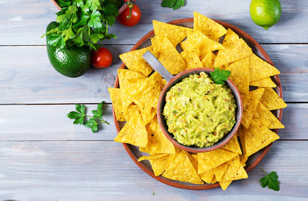 guacamole avocado, limetten, tomaten, zwiebeln und koriander, serviert mit nachos - traditionelle mexikanische snack. flach zu legen. ansicht von oben. - tortilla chip stock-fotos und bilder