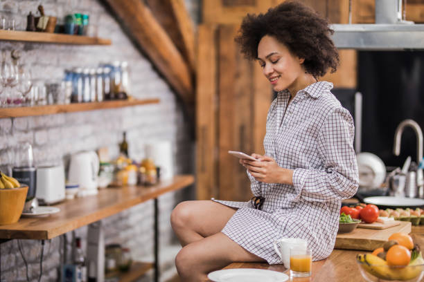 istock Happy African American woman using cell phone in the kitchen. 935958668
