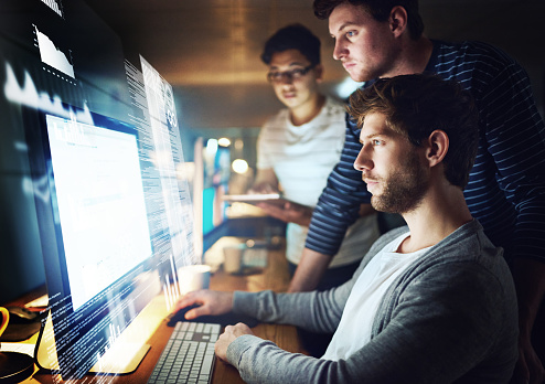 Shot of a group of programmers working on a computer code at night