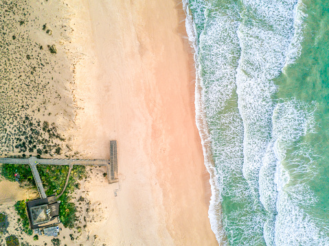 Wooden pier leading to sandy beach and waves on Atlantic Ocean in Quinta do Lago, Almancil, Algarve, Portugal