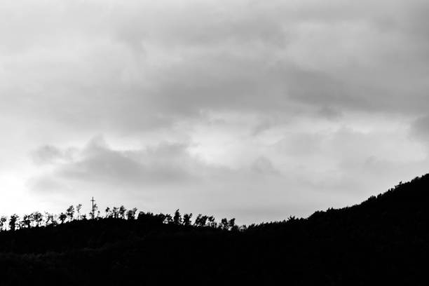 A silhouette of a hill peak at sunset, beneath sun rays coming out through clouds