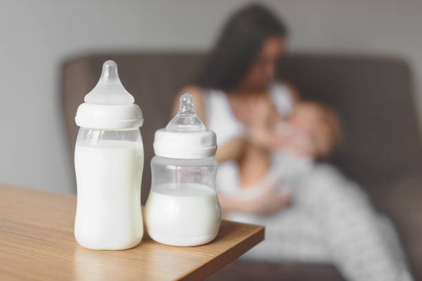 flessen met moedermelk op de achtergrond van de moeder in haar handen en borstvoeding baby houden. moederschap en baby verzorging. - gevoerd worden stockfoto's en -beelden