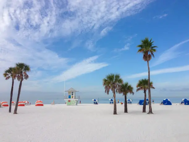 White sand beach with palm trees and lifeguard shack and colorful loungers and umbrellas.