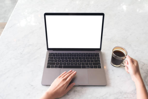 istock Top view mockup image of hands using laptop with blank white desktop screen and holding coffee cup on marble table in cafe 935978714