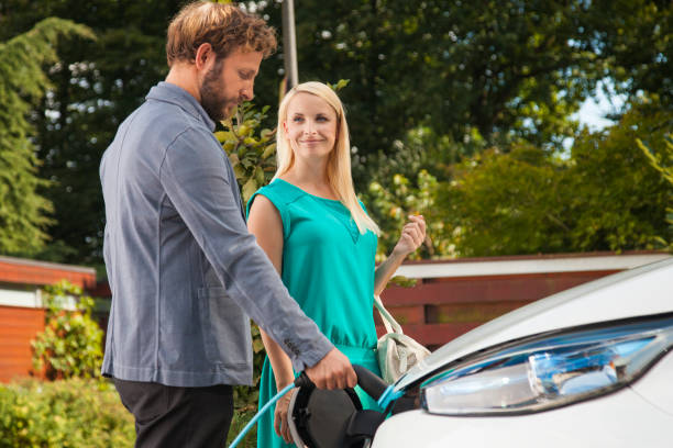 Couple charging the car before going to work Lovely couple in front of the house charging the electric car. Happy smile on woman's face. hybrid car photos stock pictures, royalty-free photos & images