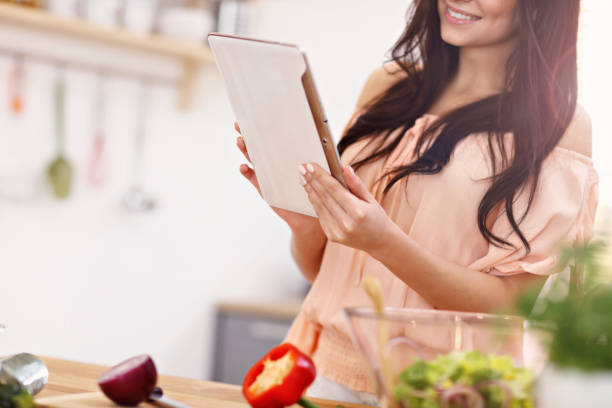 istock Happy woman preparing salad in modern kitchen and holding tablet 935984114