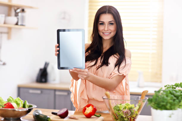 istock Happy woman preparing salad in modern kitchen and holding tablet 935985784