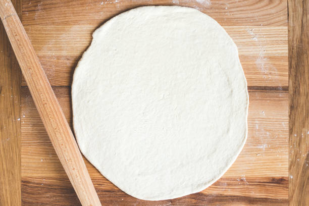 istock Raw pizza dough with wooden rolling pin 935989638
