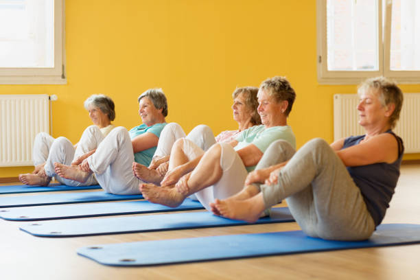 group of active senior women in yoga class exercising on mat group of active senior women in yoga class exercising on mat in yellow painted room community center photos stock pictures, royalty-free photos & images