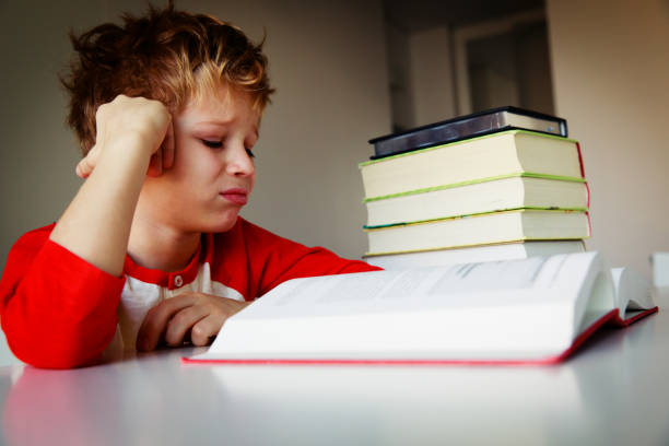 istock little boy tired stressed of reading, doing homework 935998152
