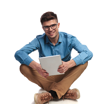 seated young casual man holding tablet on white background