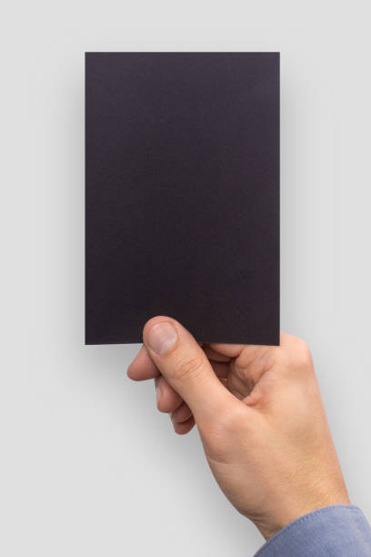 istock Mockup A6 empty blank black postcard vertically holds the man in his hand in shirt. Isolated on a gray background 936004768