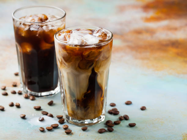istock Ice coffee in a tall glass with cream poured over and coffee beans. Cold summer drink on a blue rusty background with copy space 936008024