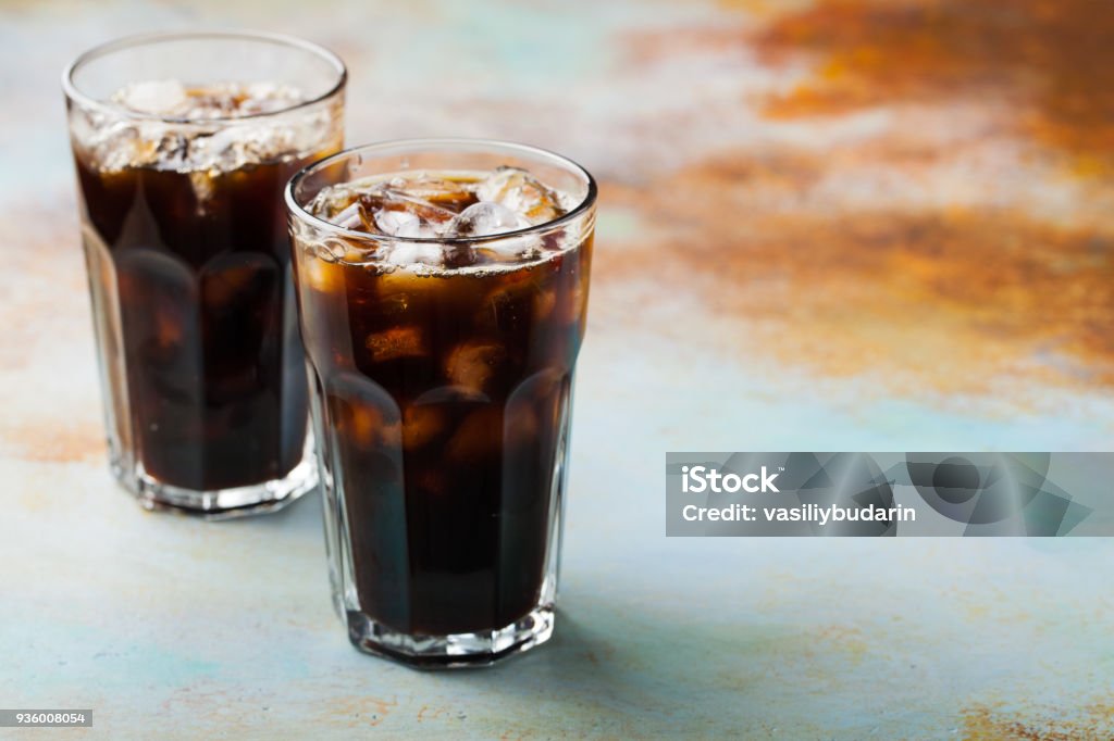 Ice coffee in a tall glass with cream poured over and coffee beans. Cold summer drink on a blue rusty background with copy space Ice coffee in a tall glass with cream poured over and coffee beans. Cold summer drink on a blue rusty background with copy space. Cola Stock Photo