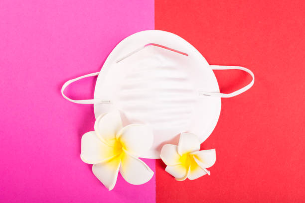 istock One face mask on pink and red background with exotic flowers 936008658