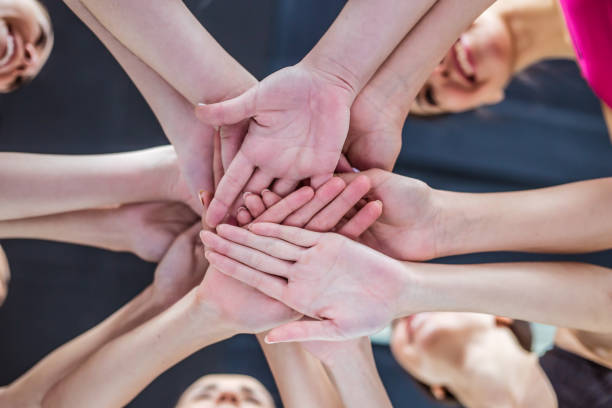 Close up photo of young smiling women putting their hands together. Close up photo of young smiling women putting their hands together. Friends with stack of hands showing unity and teamwork. community health center stock pictures, royalty-free photos & images