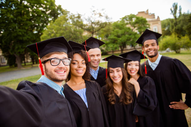 istock Selfie time! Six international students are posing for selfie shot, that nerdy guy is taking, outside school building. Gathered, cheerful, smart and successful youth in mortar boards, gowns 936016698