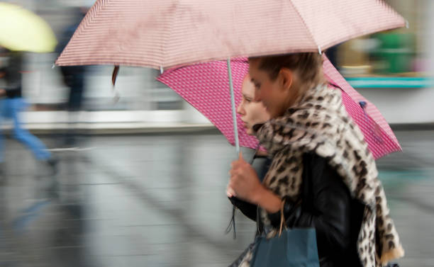 zwei junge frauen unter sonnenschirmen an einem regnerischen tag - editorial eastern europe europe reflection stock-fotos und bilder