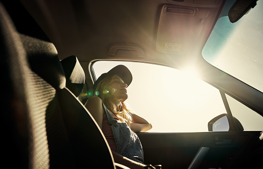 Shot of a relaxed young woman seated in a car as a passenger and taking a nap while being on the road during the day