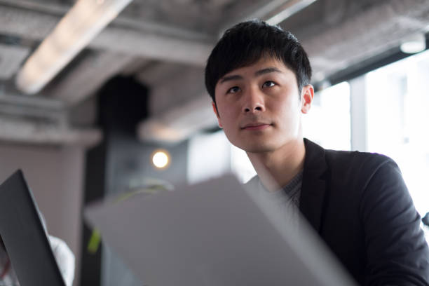 Young businessman working in co-working space Close up of Asian young businessman in co-working space common room stock pictures, royalty-free photos & images