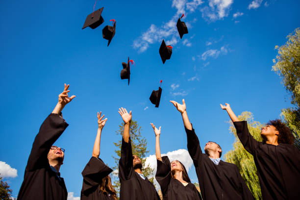 félicitations ! vue d’angle faible du joyeux groupe de six jeunes joyeux multi ethnique diplômés dans les robes noires sont vomir leurs chapeaux en l’air et célébrant, rire, profiter de - mortar board child female people photos et images de collection