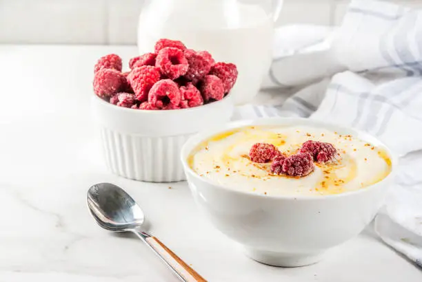Healthy breakfast, semolina porridge with milk and raspberry, white marble table copy space