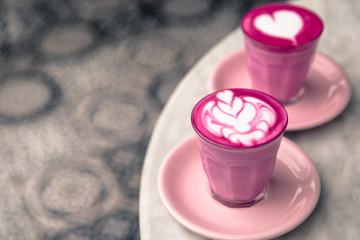 Two Beetroot latte are on standing in the pink cups and plates on white marble background. Trendy colorful red velvet drink with milk on the art floor