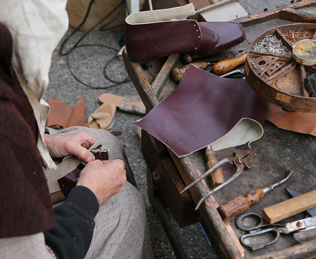 old cobbler while repairing the shoe with a piece of leather