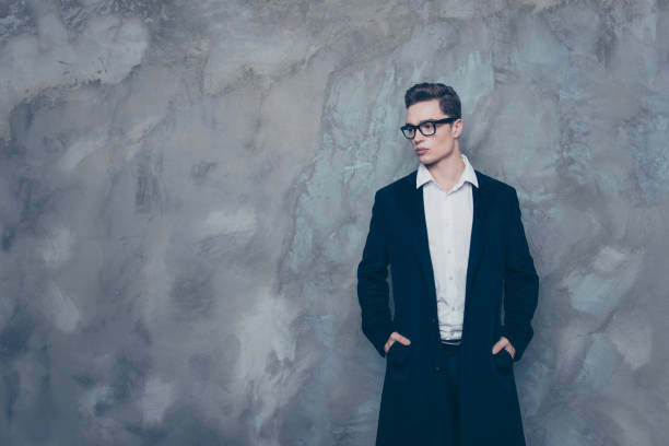 istock Handsome successful young guy in spectacles and black coat standing against gray background 936088140
