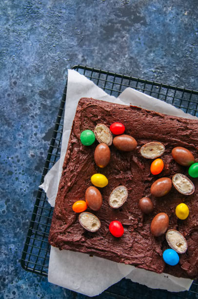 istock Dark chocolate brownie squares on a wire rack decorated with creamy chocolate eggs. Blue stone background. 936093118