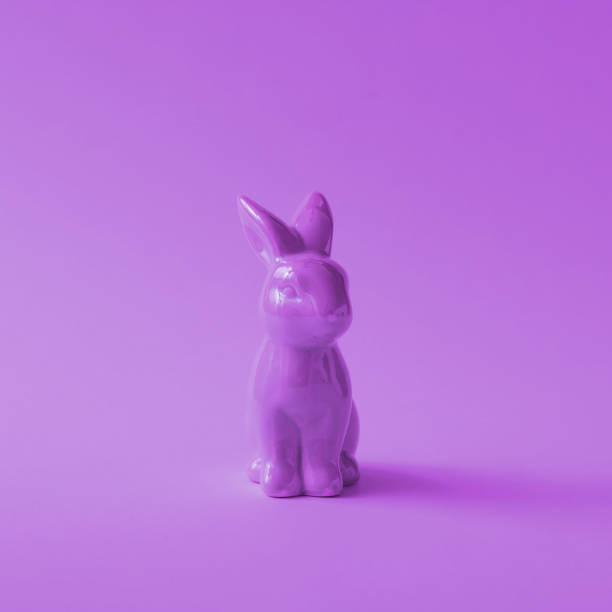 A handcrafted wooden Easter bunny decoration painted in bright colors, standing in a sunlit outdoor setting. The cute and playful design, featuring a purple dress and a cheerful expression, adds a festive and welcoming touch to the springtime celebration. The natural background enhances the warm and joyful atmosphere.