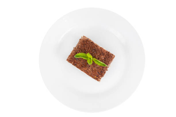 Rectangular piece of Tiramisu with a sprig of mint on a white plate. isolated on white background. Dessert for a menu in a cafe, restaurant, coffee shop view from above