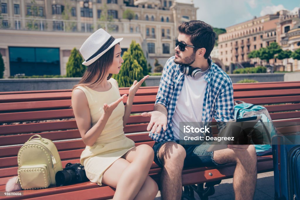 Young married couple got lost on vacation in town. Frustrated lady is arguing with her boyfriend, who holds pda, has no idea where they are Couple - Relationship Stock Photo