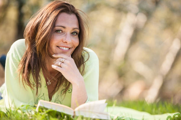 Beautiful Mature Woman Reading Book in the Spring Meadow