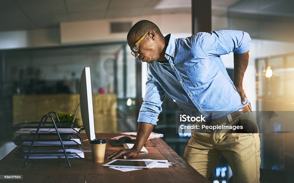 Paying the highest price for success Shot of a young businessman suffering from backache while working at his desk during a late night at work Backache Stock Photo