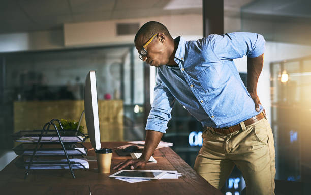 Paying the highest price for success Shot of a young businessman suffering from backache while working at his desk during a late night at work office back pain stock pictures, royalty-free photos & images