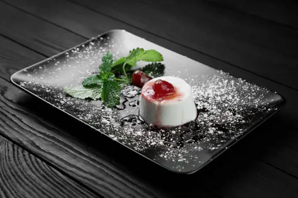 Photo of italian panna cotta dessert with strawberry sirup and mint leaf on the black wooden background