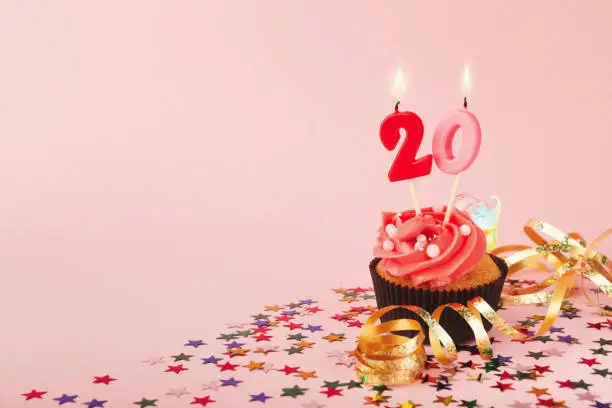 20th birthday cupcake with candles, sprinkles and ribbon on pink background. Card mockup, copy space. Birthday, party, holiday concept