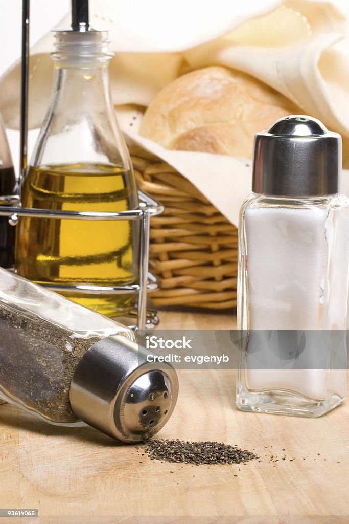 Bread, olive oil and spices Pepper pot with black pepper, fresh bread, bottle of olive oil and spicy herbs on wooden cut board Antipasto Stock Photo