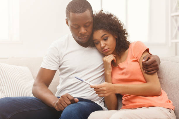 Sad black couple after pregnancy test result Sad african-american couple after negative pregnancy test result, sitting on couch at home, copy space infertility stock pictures, royalty-free photos & images