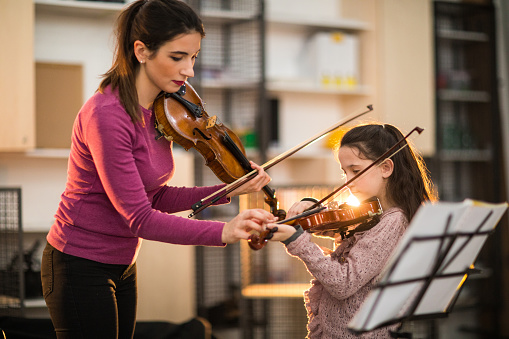 Young woman teaching her child student to play the violin