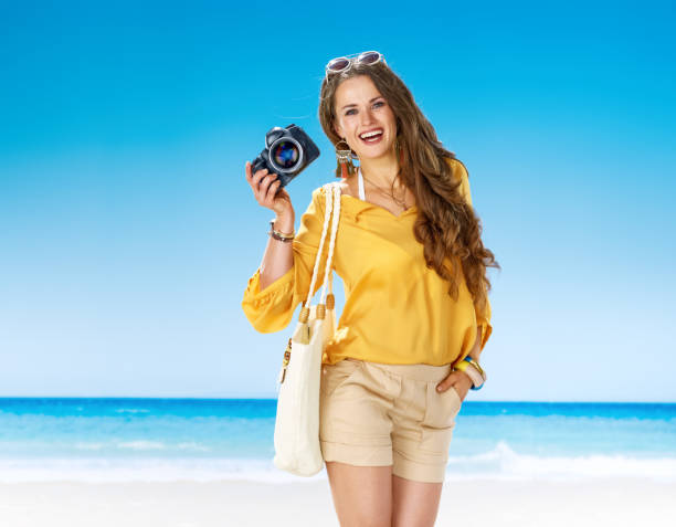smiling active woman on seacoast showing digital SLR camera