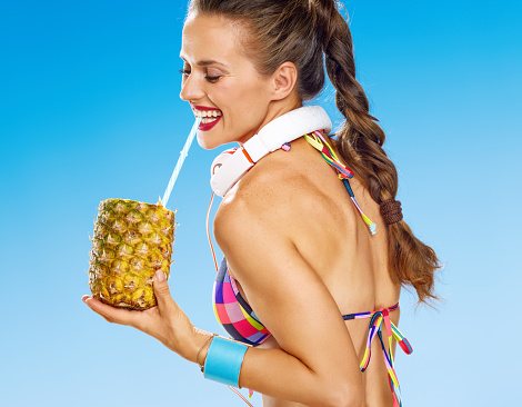 woman on seacoast drinking refresh beverage from pineapple